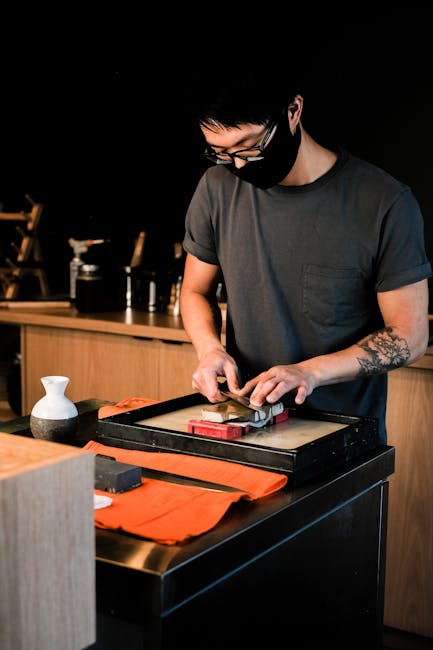 A man with dark hair and glasses, wearing a black T-shirt, is inside a home preparing for a move. He is standing near a wooden countertop, using a hammer and a metal tool to assemble or disassemble furniture or packing materials. The background shows kitchen cabinets and a window that allows natural light into the room. The workspace is organized, and the man appears focused on his task, which is part of a home relocation or packing process. This scene exemplifies key stages in furniture assembly or disassembly during house removals, highlighting the attention to detail required in professional moving services offered by Man with Van Whetstone, supporting the logistical aspects of packing and furniture transport.