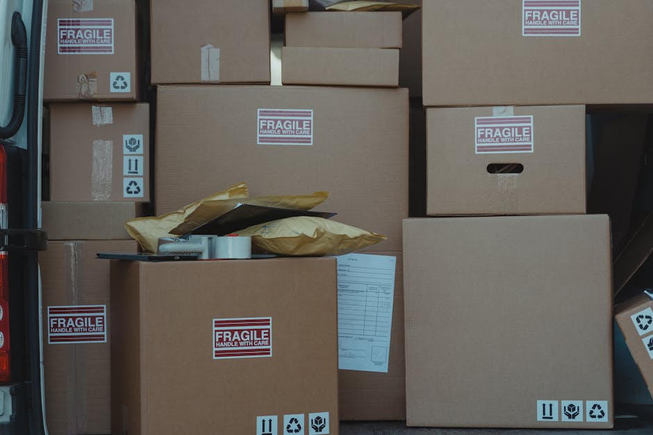 The image shows the open rear of a moving van filled with various cardboard boxes of different sizes, some sealed with packing tape and others slightly opened, revealing paper or packaging materials i