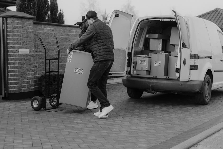 The image shows the open rear of a moving van filled with various cardboard boxes of different sizes, some sealed with packing tape and others slightly opened, revealing paper or packaging materials i